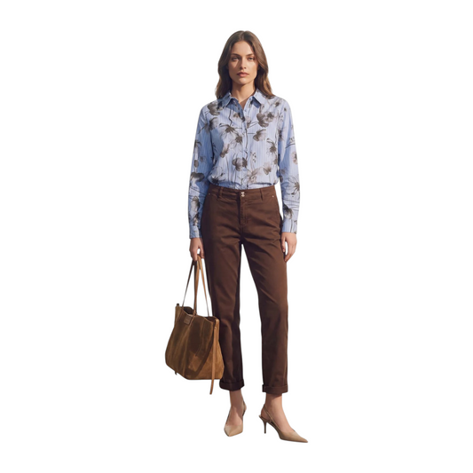 Modella indossa camicia a righe azzurre con stampa floreale, abbinata a pantaloni marroni e borsa in pelle